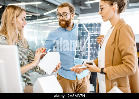 Young group of engineers working on a project of alternative energy in the office, holding model of house, wind turbine and solar panel Stock Photo