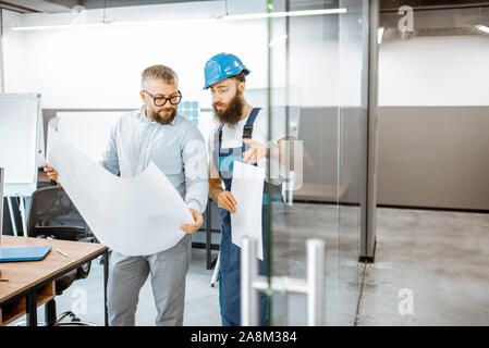 Senior foreman and workman in overalls working on project with blueprints in the office