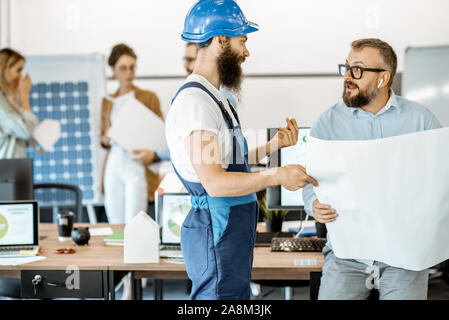 Senior foreman and workman in overalls working on project with blueprints in the office Stock Photo