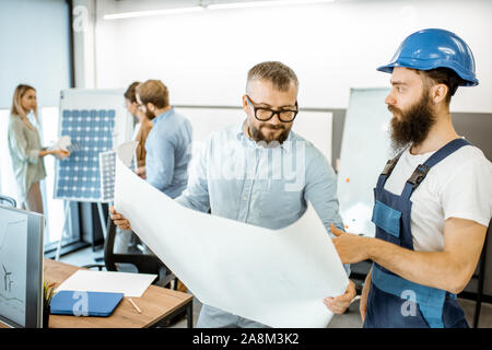 Senior foreman and workman in overalls working on project with blueprints in the office Stock Photo