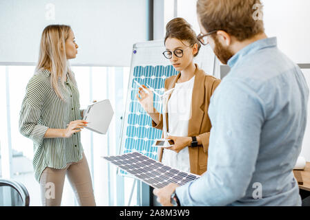 Young group of engineers working on a project of alternative energy in the office, holding model of house and solar panel Stock Photo