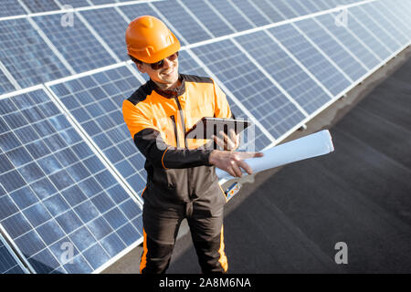 Portrait of an engineer in protective workwear carrying out service of solar panels with digital tablet and blueprintson a photovoltaic rooftop plant Stock Photo