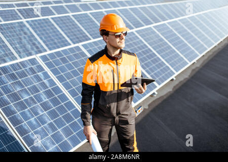 Portrait of an engineer in protective workwear carrying out service of solar panels with digital tablet and blueprintson a photovoltaic rooftop plant Stock Photo