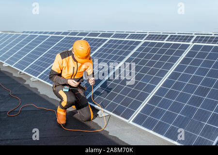 Well-equipped electrician connecting solar panels, checking the voltage and connecting wiring on a rooftop photovoltaic power plant Stock Photo