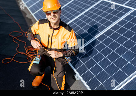 Well-equipped electrician connecting solar panels, checking the voltage and connecting wiring on a rooftop photovoltaic power plant Stock Photo