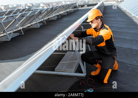 Well-equipped electrician connecting wires of solar panels on a rooftop photovoltaic power plant. Concept of installing solar stations Stock Photo