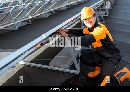 Well-equipped electrician connecting wires of solar panels on a rooftop photovoltaic power plant. Concept of installing solar stations Stock Photo