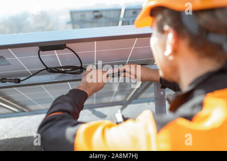 Electrician connecting wires of solar panels on a rooftop photovoltaic power plant. Concept of installing solar stations Stock Photo
