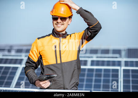 Portrait of a well-equipped worker in protective orange clothing servicing solar panels on a photovoltaic plant. Concept of maintenance and installation of solar stations Stock Photo