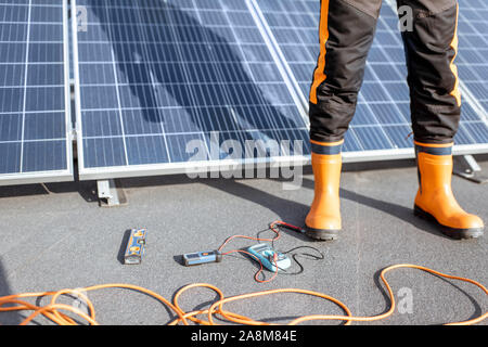 Installing solar panels, close-up on a working tools. wires and man in protective clothing standing on a rooftop with photovoltaic power station Stock Photo
