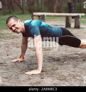 Athletic man smiling while doing pushups outdoor Stock Photo