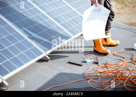 Installing solar panels, close-up on a working tools. wires and man in protective clothing standing on a rooftop with photovoltaic power station Stock Photo