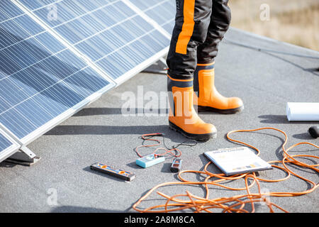 Installing solar panels, close-up on a working tools. wires and man in protective clothing standing on a rooftop with photovoltaic power station Stock Photo