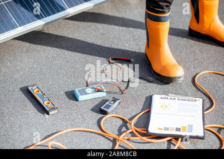 Installing solar panels, close-up on a working tools. wires and man in protective clothing standing on a rooftop with photovoltaic power station Stock Photo