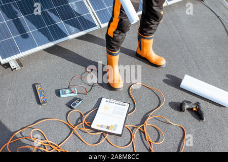 Installing solar panels, close-up on a working tools. wires and man in protective clothing standing on a rooftop with photovoltaic power station Stock Photo
