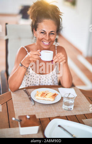 Middle age beautiful woman sitting on terrace drinking cup of coffe smiling Stock Photo