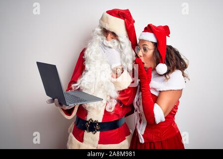 Senior couple wearing Santa Claus costume using laptop over isolated white background cover mouth with hand shocked with shame for mistake, expression Stock Photo