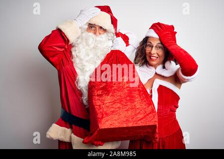 Senior couple wearing Santa Claus costume holding sack over isolated white background stressed with hand on head, shocked with shame and surprise face Stock Photo