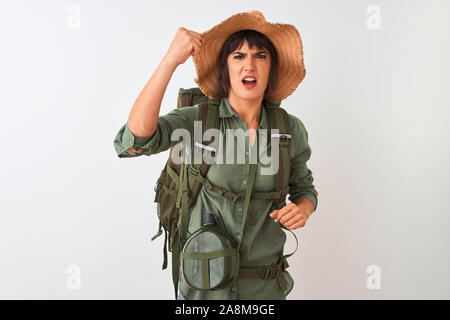 Hiker woman wearing backpack hat and water canteen over isolated white background angry and mad raising fist frustrated and furious while shouting wit Stock Photo