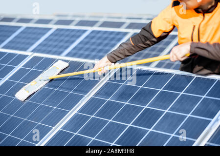 Professional cleaner in protective workwear cleaning solar panels with a mob. Concept of solar power plant cleaning service Stock Photo