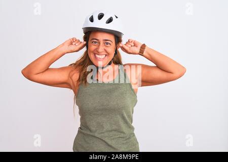 Middle age mature cyclist woman wearing safety helmet over isolated background Smiling pulling ears with fingers, funny gesture. Audition problem Stock Photo