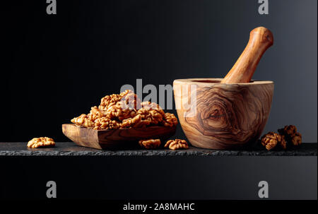 Walnuts in wooden dish and mortar with pestle on a black background. Copy space. Stock Photo
