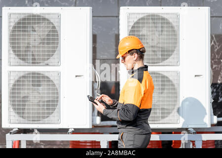 Professional workman in protective clothing adjusting the outdoor unit of the air conditioner or heat pump with digital tablet Stock Photo