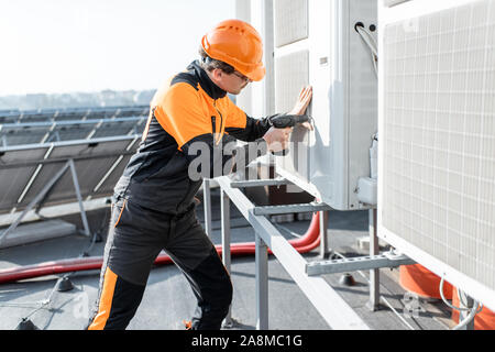 Professional workman in protective clothing installing or reparing outdoor unit of the air conditioner or heat pump on the rooftop Stock Photo