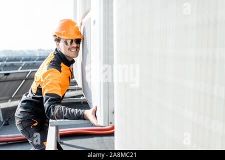 Professional workman in protective clothing installing outdoor unit of the air conditioner or heat pump on the rooftop Stock Photo