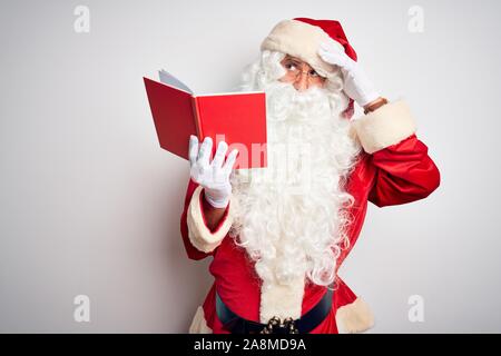 Middle age man wearing Santa Claus costume reading book over isolated white background worried and stressed about a problem with hand on forehead, ner Stock Photo