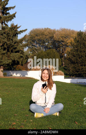 happy teenage girl listens to music from her smartphone in park autumn season Stock Photo