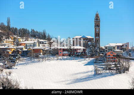 Houses ans church with tall belfry in small town of Monforte d'Alba on the hill covered in snow in Piedmont, Northern Italy.