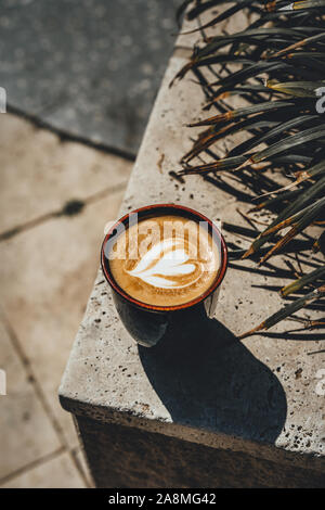 Heart latte coffee art in ceramic cup on a marble tile outdoors. Stock Photo