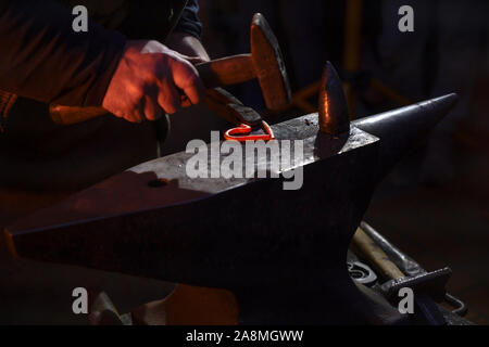 Blacksmith forges a hot glowing iron heart with a hammer on the anvil, symbol of eternal love, dark background, copy space, selected focus, narrow dep Stock Photo