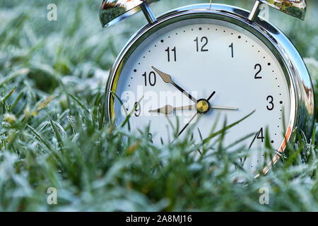 The alarm clock is in the grass covered with frost Stock Photo