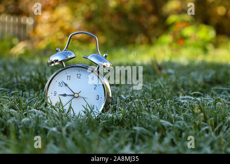The alarm clock is in the grass covered with frost Stock Photo