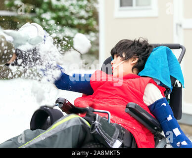 Little disabled boy in wheelchair outside playing with snow in winter Stock Photo