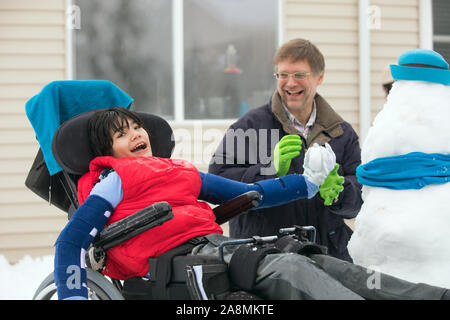 Father playing with disabled son in wheelchair  outdoors in the snow, throwing snowballs in winter outdoors Stock Photo