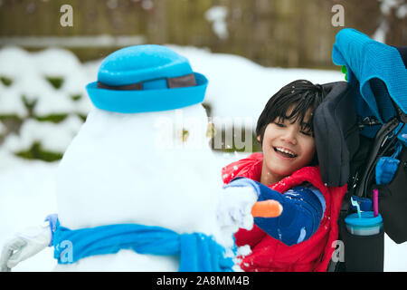 Smiling, happy little boy in wheelchair outdoors in winter having fun building a snowman Stock Photo