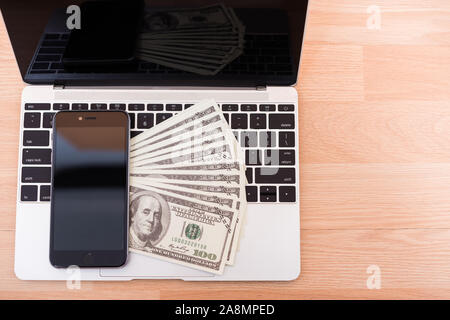 Top view laptop computer, dollar bill and smartphone blank screen on keyboard at office desk table, finance concept Stock Photo