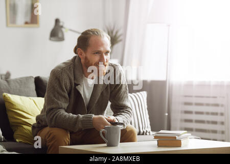 Portrait of smiling bearded man watching TV at home and holding remote control, copy space Stock Photo
