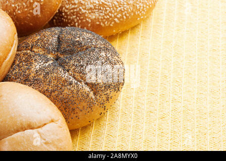 Assorted Kaiser rolls on a yellow colored textured placemat. Fresh bread includes poppy seed rolls and sesame seed buns and plain with no seeds Stock Photo