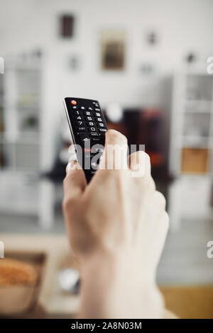 Close up of male hand holding TV remote against big screen television set, copy space Stock Photo