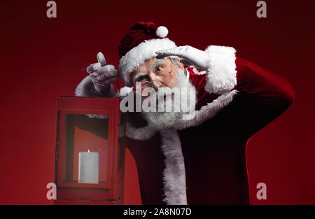 Waist up portrait of fairytale Santa Claus holding lantern standing against red background in studio Stock Photo