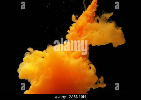 Abstract flowing liquid or orange color ink in water on a black background. It looks like smoke or cloud. Or zero gravity. Stock Photo