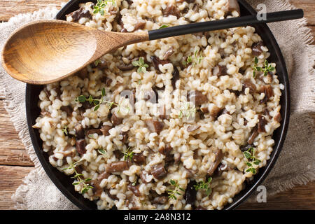 Traditional Orzotto (perlotto) with forest porcini mushrooms and thyme closeup on a plate on the table. Horizontal top view from above Stock Photo