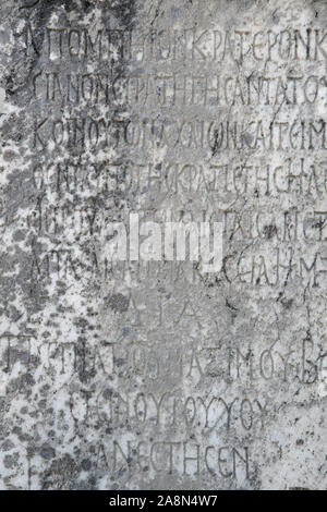 Half-erased ancient Greek letters embossed on an old gray marble slab covered with cracks and mold. Stock Photo