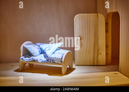 Doll plywood bed with blankets and pillows in the dollhouse. Miniature. Stock Photo