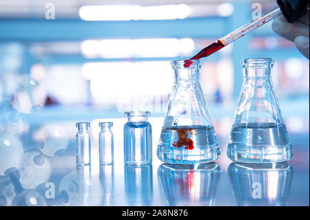 orange drop in glass flask with vial and chemical molecular on blue chemistry science laboratory background Stock Photo