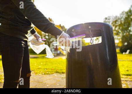 Volunteer putting straws in garbage bin at park Stock Photo